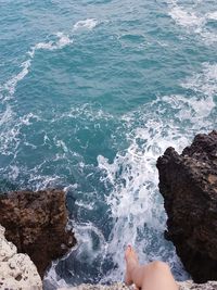 Low section of woman sitting on rock over sea