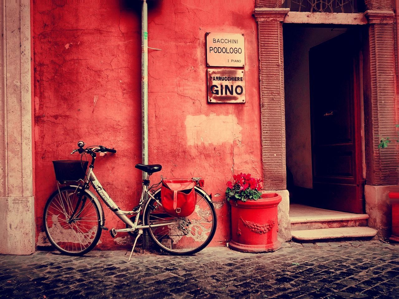 building exterior, red, architecture, built structure, bicycle, wall - building feature, house, parked, stationary, transportation, potted plant, wall, door, outdoors, parking, closed, day, brick wall, no people, flower