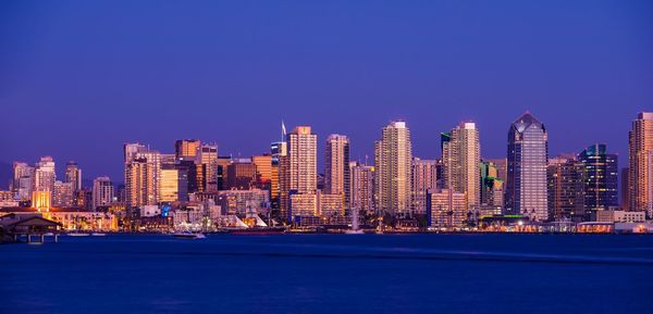 Illuminated cityscape against clear blue sky at night