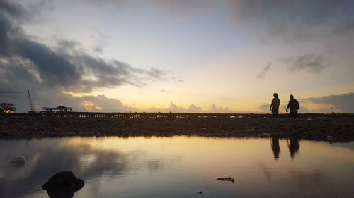 Silhouette people on lake against sky during sunset