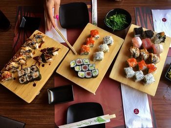 High angle view of women holding chopsticks with sushi on cutting boards