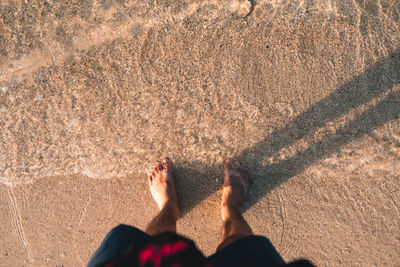 Low section of man standing at sea shore