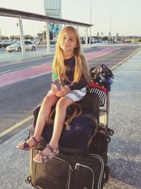 Portrait of smiling girl holding water bottle while sitting on luggage bags