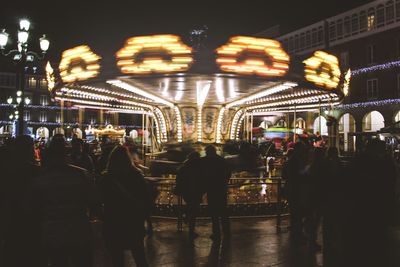 People at illuminated carousel in amusement park