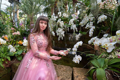 Portrait of beautiful woman standing by flowering plants