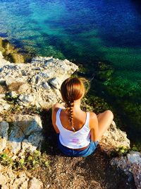 Rear view of woman sitting on rock by sea