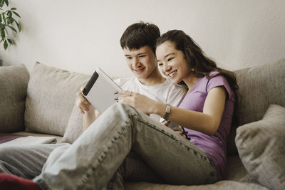 Excited male and female siblings sharing digital tablet while sitting on sofa at home