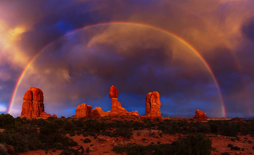 View of rainbow over rocks against cloudy sky