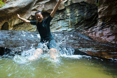 Cheerful woman jumping in pond by rock formation