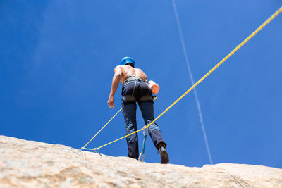 Rear view of shirtless man climbing rock