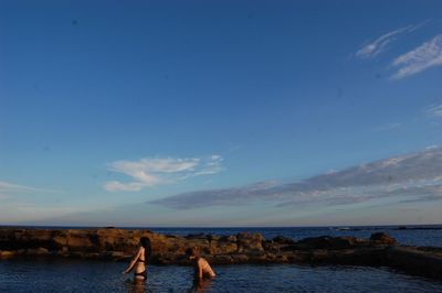 Friends playing in lake against blue sky