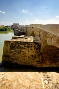 Arch bridge over river against cloudy sky