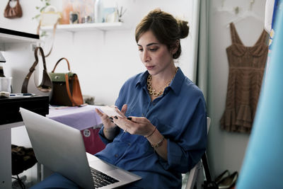 Female owner using smart phone while working in clothing store