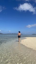 Rear view of woman walking at beach against sky