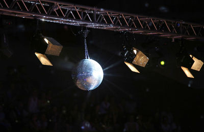 Low angle view of illuminated lights and shiny disco ball hanging from ceiling