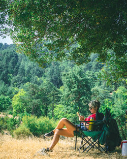 Woman sitting on land against trees