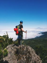 Rear view of hiker on rock looking at clouds covered landscape against sky