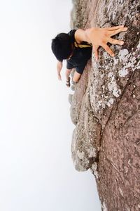 Tilt shot of young man lying on rock against clear sky