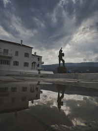 Man standing on statue by building against sky