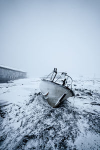 Abandoned boat on snow covered shore against clear sky