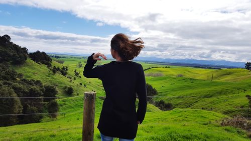 Rear view of woman photographing on field against sky