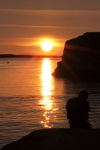 Silhouette people looking at sea against sky during sunset