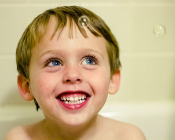 Up close of smiling boy in bathtub watching bubbles float