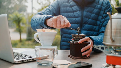 Close up man hand grinding coffee beans with manual stainless steel grinder to make drip coffee