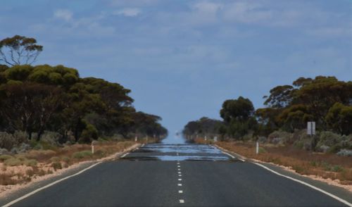 Empty road amidst trees against sky