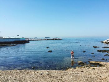 Rear view of man standing in sea against clear sky