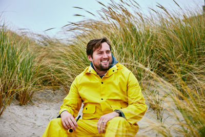 Smiling man sitting at beach against sky