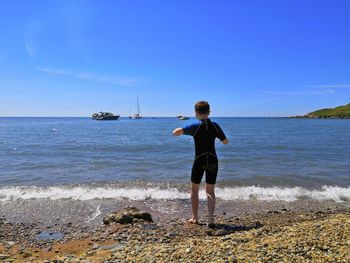 Rear view of boy standing at beach against sky