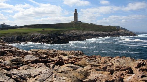 Lighthouse on hill by sea against sky