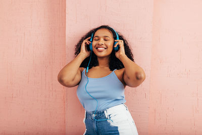 Young woman listening music against wall