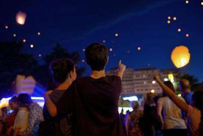 People looking at lit paper lanterns against sky