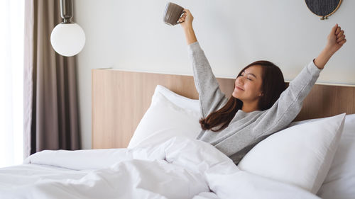 Low angle view of young woman using mobile phone while lying on bed at home