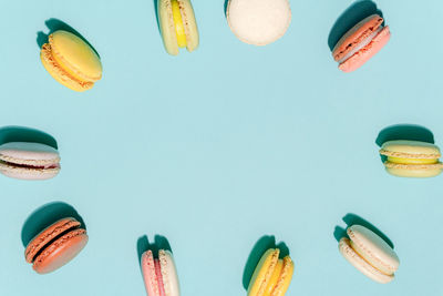 French dessert concept, circle arrangement of colorful pastel macarons on light blue background.