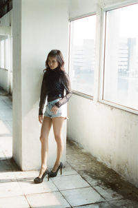 Full length portrait of woman standing against window