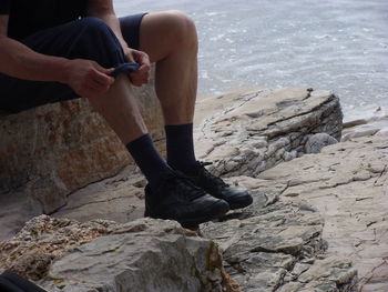 Low section of man folding pants on rock at beach