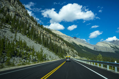 Road with yellow line by mountain against sky and car with yellow cayaks in canada.