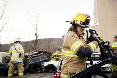 Female firefighter cutting car while standing against clear sky