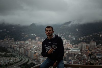 Portrait of young man standing in city against sky