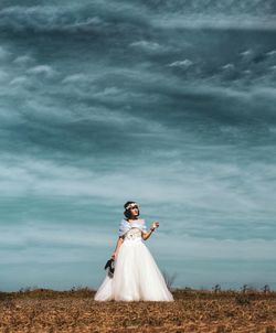 Woman with umbrella standing on field against sky