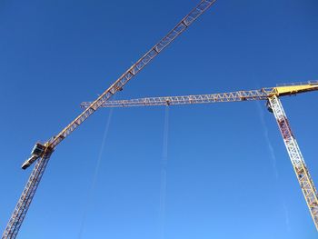 Low angle view of cranes against blue sky