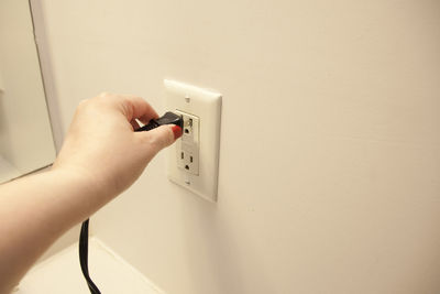 Close-up of hand holding mobile phone against wall