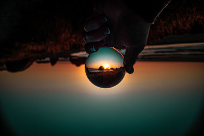 Close-up of hand holding illuminated light against sky during sunset