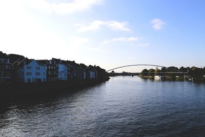 Bridge over river by buildings against sky