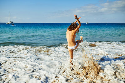 Full length of young woman jumping in sea against sky