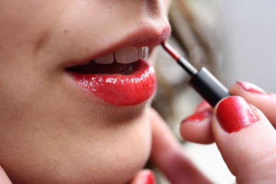 Close-up of young woman applying red lipstick