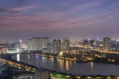 Illuminated buildings by river against sky at night